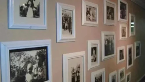 A wall covered in various sized black and white framed photos, with white frames, hanging on a beige wall